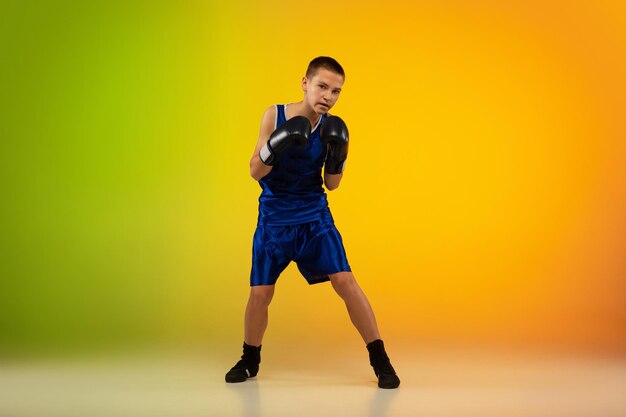 Teenage boxer against gradient neon studio in motion of kicking, boxing