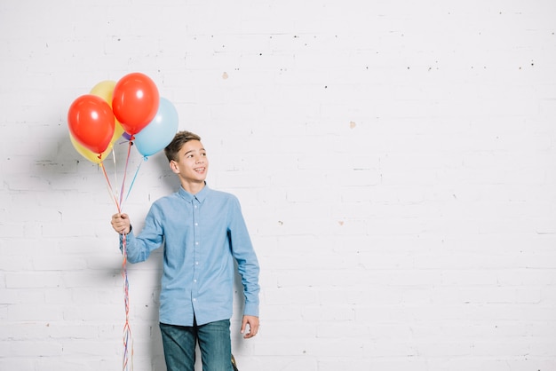 Teenage boy holding balloons in hand looking away