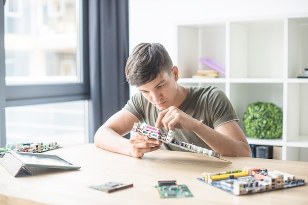 Free photo teenage boy repairing the computer motherboard on the wooden desk