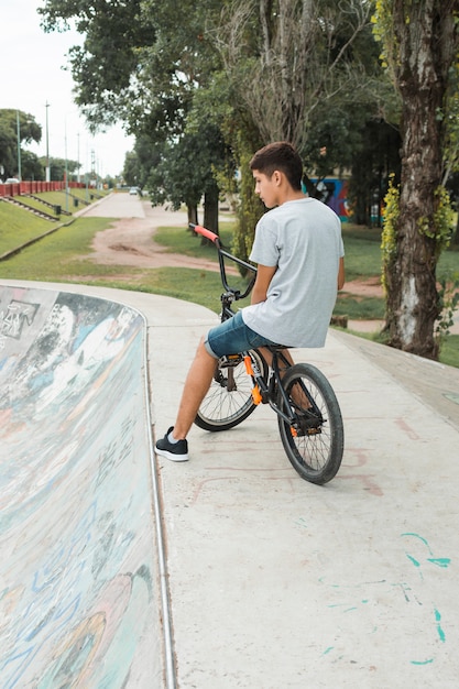 Teenage boy sitting on bicycle over the concrete skate park