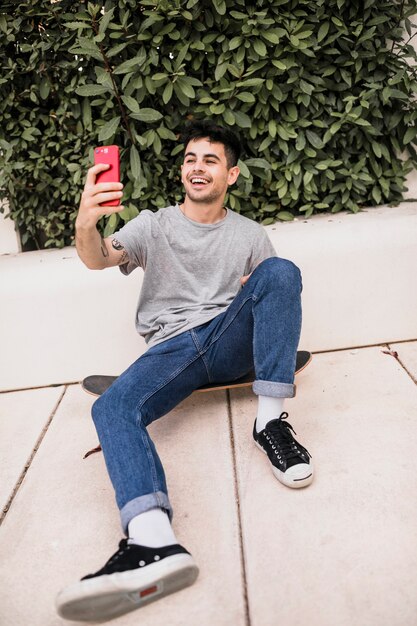 Teenage boy sitting on skateboard taking selfie with mobile phone