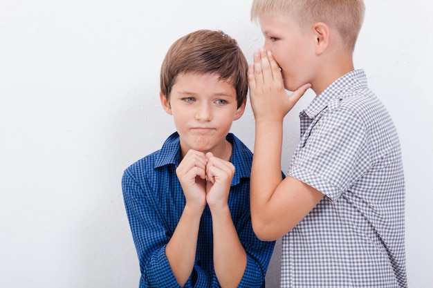 Teenage boy whispering in the ear a secret to friend on white  wall