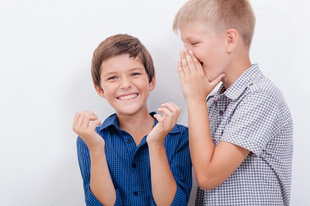 Teenage boy whispering in the ear a secret to friend on white  wall