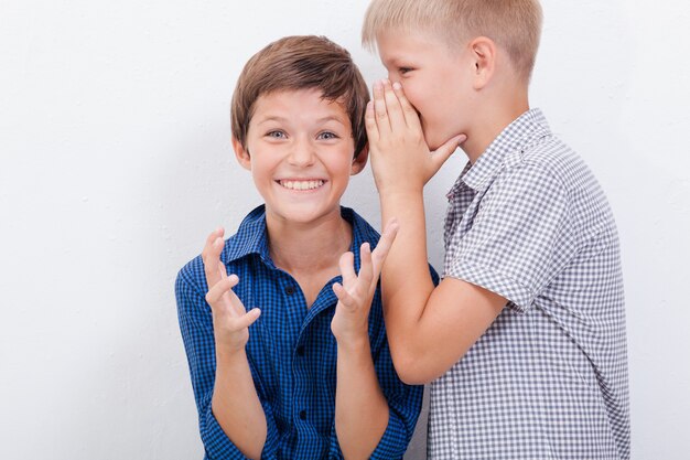 Подросток шепчет секрет на ухо удивленному другу на белом фоне
