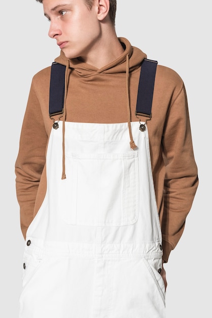 Free photo teenage boy in white dungarees and brown hoodie streetwear photoshoot