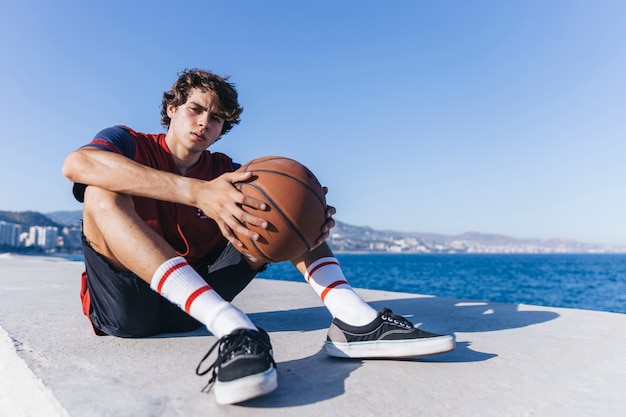 Teenage boy with basketball sitting near sea