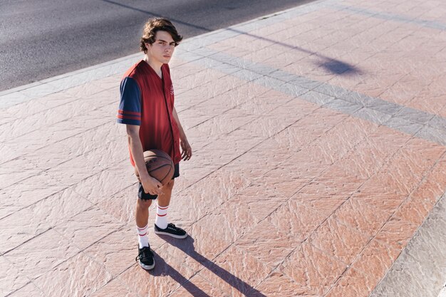 Teenage boy with basketball standing on sidewalk