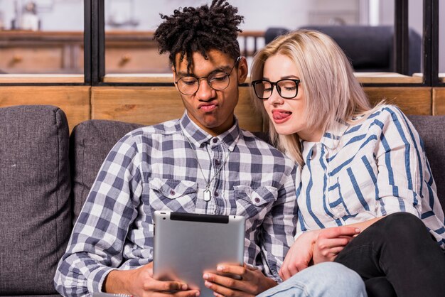 Teenage couple sitting together on sofa looking at digital table