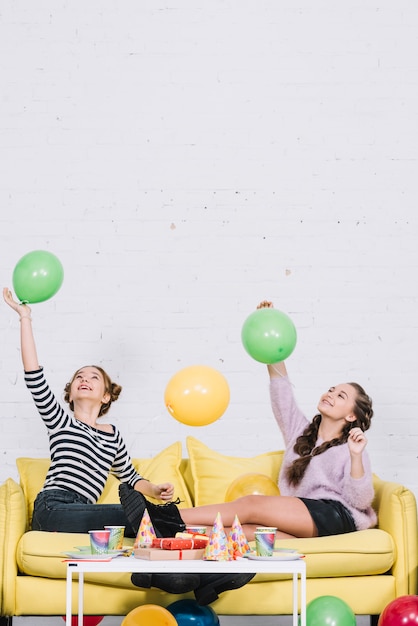 Бесплатное фото Подростковые подруги, сидя на диване, играя с воздушными шарами в день рождения