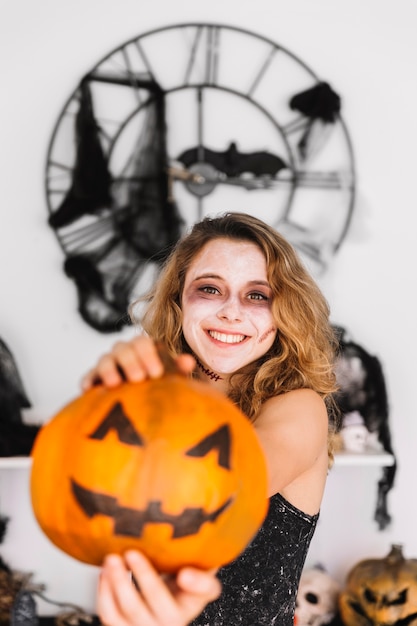 Teenage girl in alloween decorations holding pumpkin and smiling