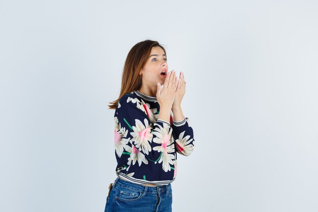 Teenage girl in blouse, jeans with hands near mouth and looking puzzled , front view.