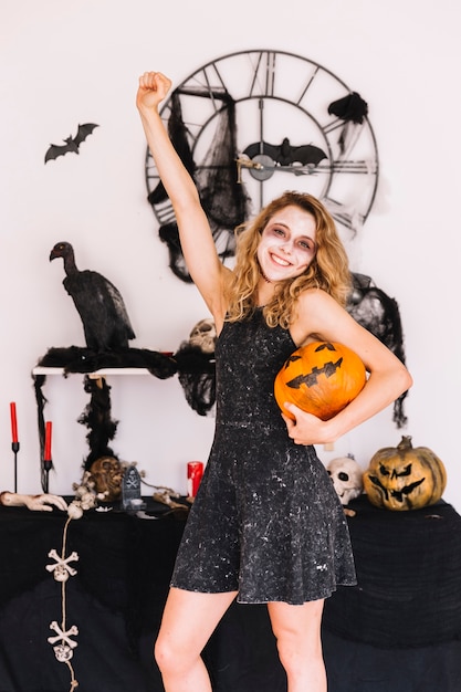 Free photo teenage girl in dark dress and grim in front of halloween decorations