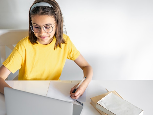 Девочка-подросток делает домашнее задание, сидя с книгами и ноутбуком