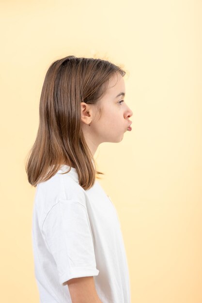 Foto gratuita un'adolescente fa le grimace con le labbra strette in un tubo su uno sfondo giallo