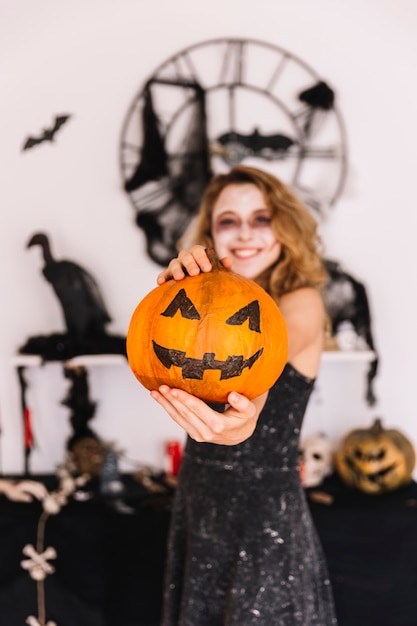 Teenage girl in Halloween decorations holding pumpkin and smiling