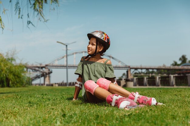헬멧에 십 대 소녀는 화창한 여름 날에 균형 또는 롤러 블레이드를 들고 롤러 스케이트를 타고 도시의 거리에서 회전하는 법을 배웁니다.