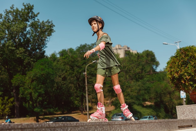 Free photo teenage girl in a helmet learns to ride on roller skates outdoors