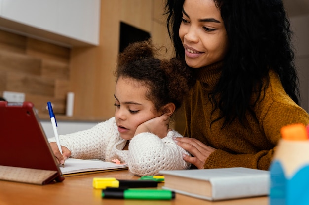 Teenage girl helping little sister during online school with tablet