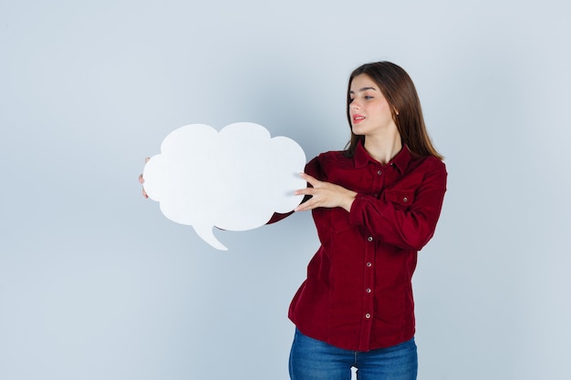 Teenage girl holding speech bubble in burgundy shirt and looking confident , front view.