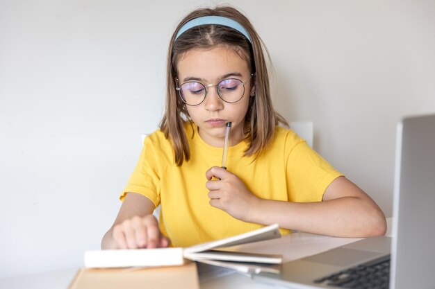 A teenage girl is doing homework with books and a laptop sitting at a table