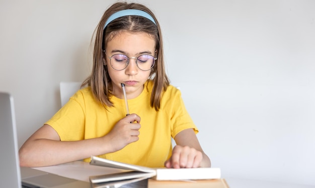 Девочка-подросток делает домашнее задание с книгами и ноутбуком, сидя за столом