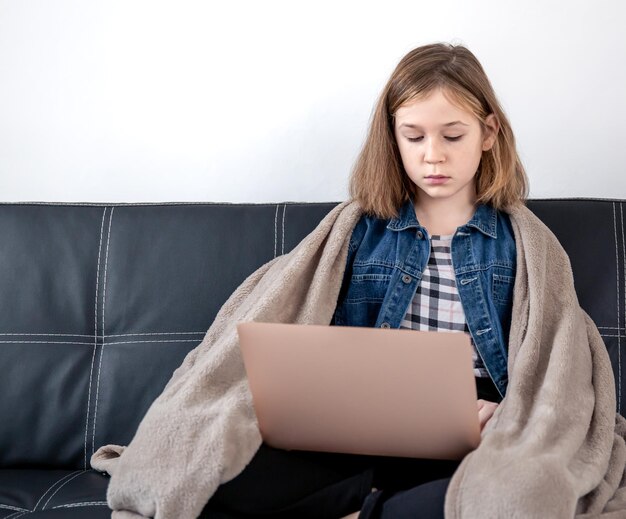 10代の少女は、格子縞に包まれたラップトップでソファに座っています