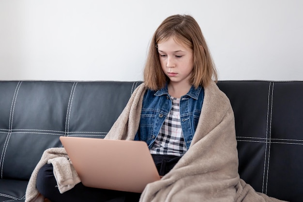 A teenage girl is sitting on the couch with a laptop wrapped in a plaid