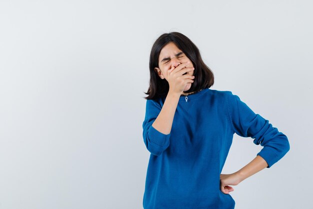 The teenage girl is yawning by covering mouth with hand  on white background