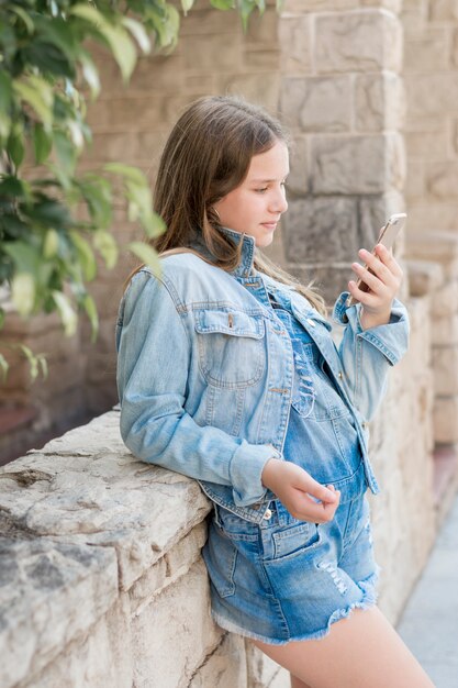 Teenage girl leaning on wall looking at cellphone