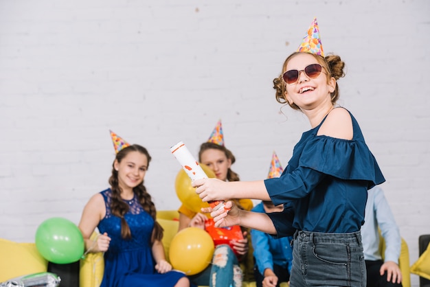 A teenage girl letting off party popper standing in front of her friends enjoying the party