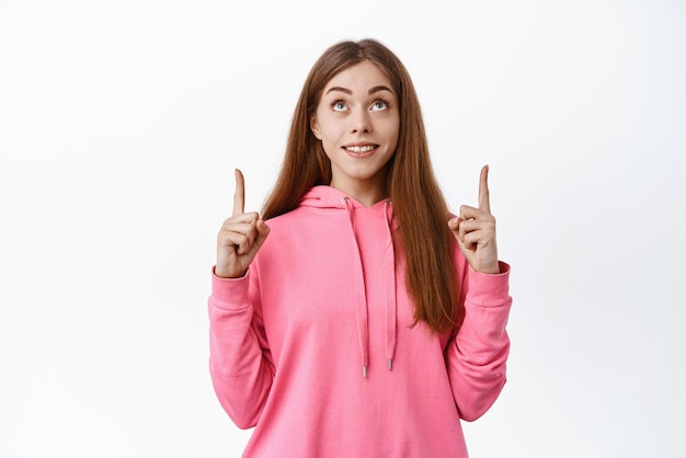 Teenage girl look with hopeful face on top smiling and pointing fingers up standing in casual clothes against white background