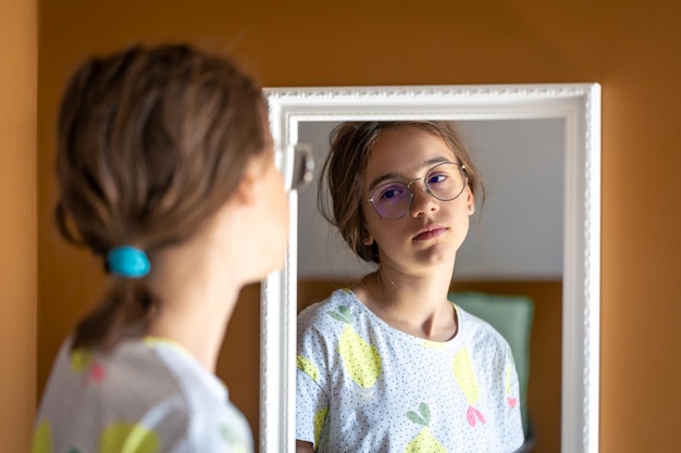 A teenage girl looks at herself in the mirror in the morning