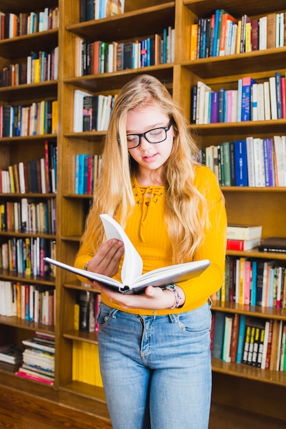 Teenage girl reading book standing at shelves
