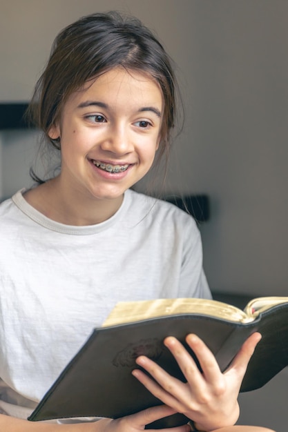 Free photo a teenage girl reads a book and smiles showing her teeth with braces