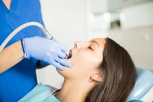 Teenage girl receiving treatment with dental tool from dentist in clinic