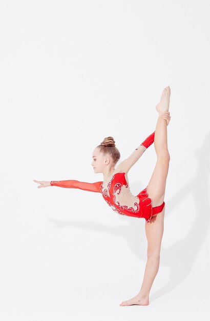 Teenage girl in red dress doing gymnastic exercises on light background.