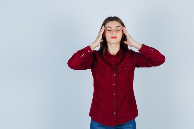 Teenage girl rubbing temples in burgundy shirt and looking relaxed. front view.