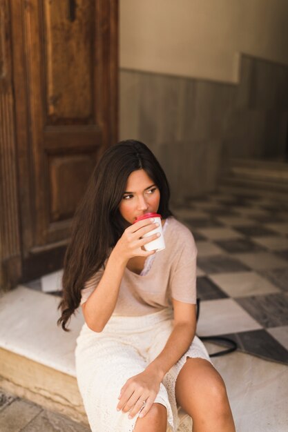 Девочка-подросток, сидящая на пороге, пить кофе из чашки
