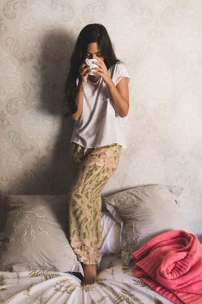 Девочка-подросток, стоя на кровати, пить кофе