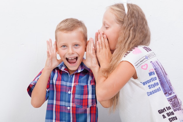 Teenage girl whispering in the ear of a secret teen boys on white  background