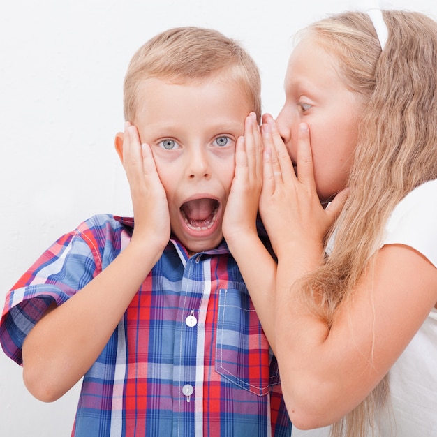 Free photo teenage girl whispering in ear of a secret teen boys on white