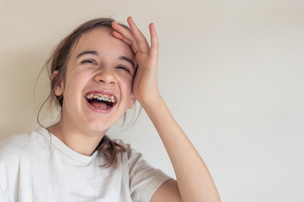 A teenage girl with braces smiles against the background of a white wall