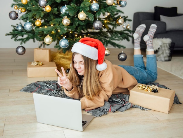 Teenage girl with gifts and laptop near the christmas tree. living room interior with christmas tree and decorations. new year. gift giving.