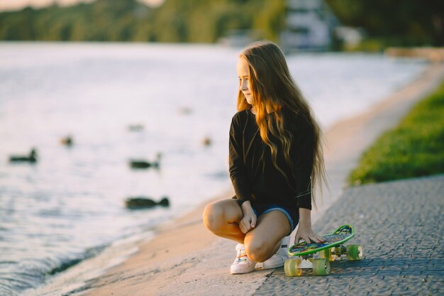 湖のそばに座っているスケートボードを持つ10代の少女