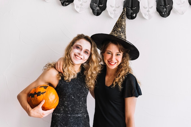 Teenage girls in alloween costumes and pumpkin hugging