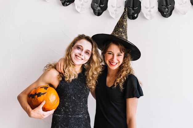 Teenage girls in alloween costumes and pumpkin hugging
