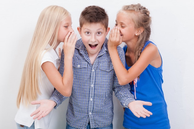 Teenage girsl whispering in the ears of a secret teen boy on white  background