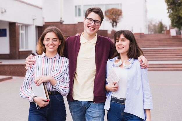 Foto gratuita ragazzo adolescente studente abbracciando compagni di classe ragazza e guardando la telecamera