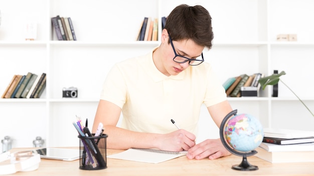 Foto gratuita studente adolescente con gli occhiali seduto al tavolo e scrivere