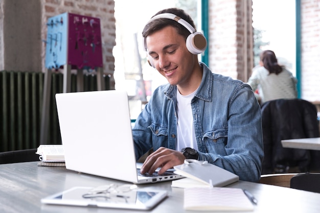 Teenage student in headphones sitting at table and typing on notebook 